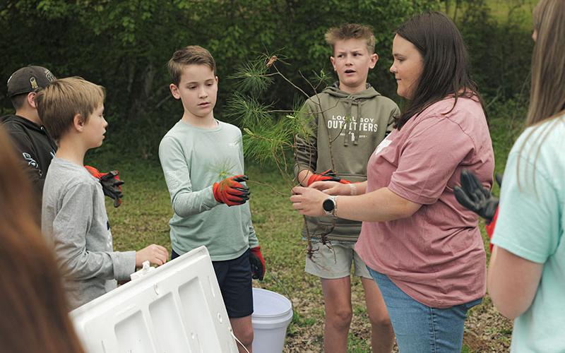 Emily Owenby of Noontootla Creek Farms passes out trees to students, from left, Tyler Jarrett, Lukas Pack, and Braxton Ballew