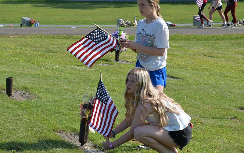 Emery Collins, standing, and Ayla Walton are listening to specific instructions as Ayla places a flag at the headstone of a veteran in J.P. Chastain Memorial Park. Fannin County Middle School students placed nearly 400 flags last Wednesday.