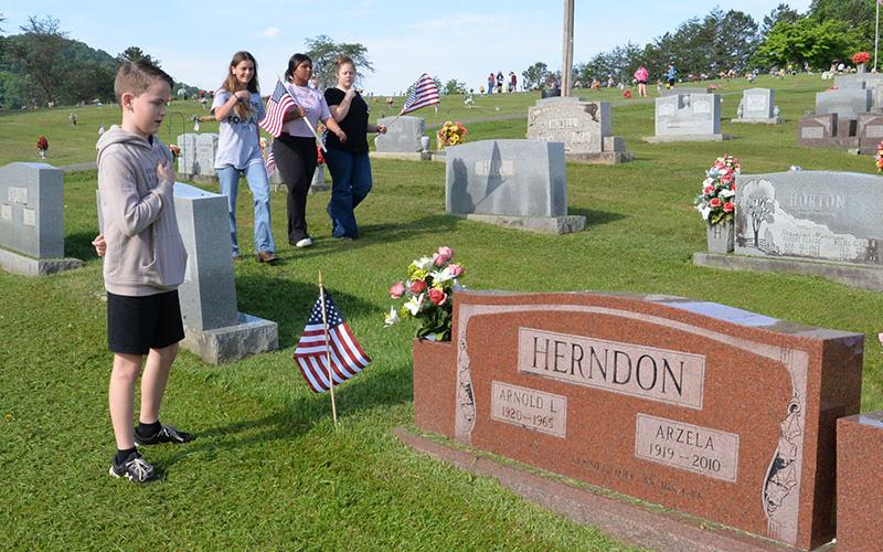 Lukas Pack shows his respect for a deceased veteran as Mackenzie Duvall, Emma Chambers and Lauren Waters search a row of headstones for a veteran to honor. All are students at Fannin County Middle School.