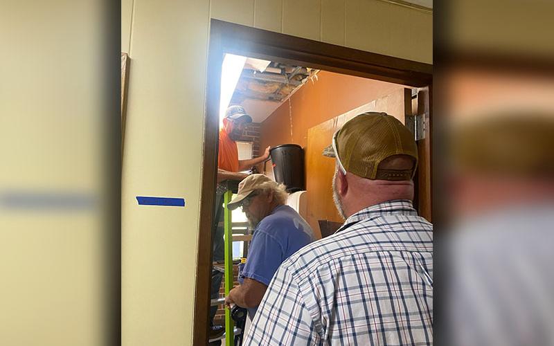 County Executive Robby Hatcher, back to camera, watches as workmen collect water draining from the community center ceiling.