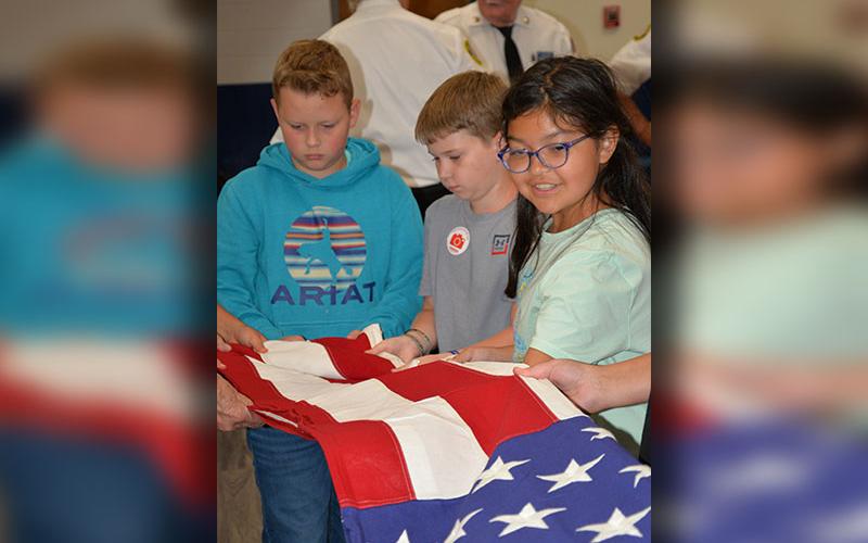 Levi White, Brantley Barton and Isabella Castro, from left, learn how to properly fold a U.S. flag from members of the North Georgia Honor Guard.