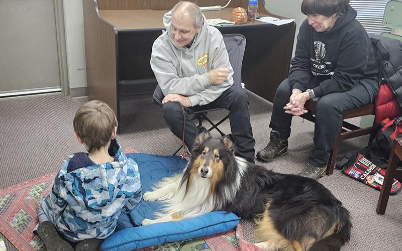 Leon Painter practices his reading skills with Calder at the Fannin County Public Library’s Book Buddies with Calder Reading Dog Program. Calder’s handlers Bill and Lois Hall are also shown.