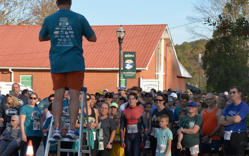 Matt Cole, atop ladder, gets racers ready for the November 2 Bigfoot Boogie, which drew the largest number of registrants yet to the Riverwalk Run Series. Cole created the series five years ago with the Bigfoot Boogie as the first race.