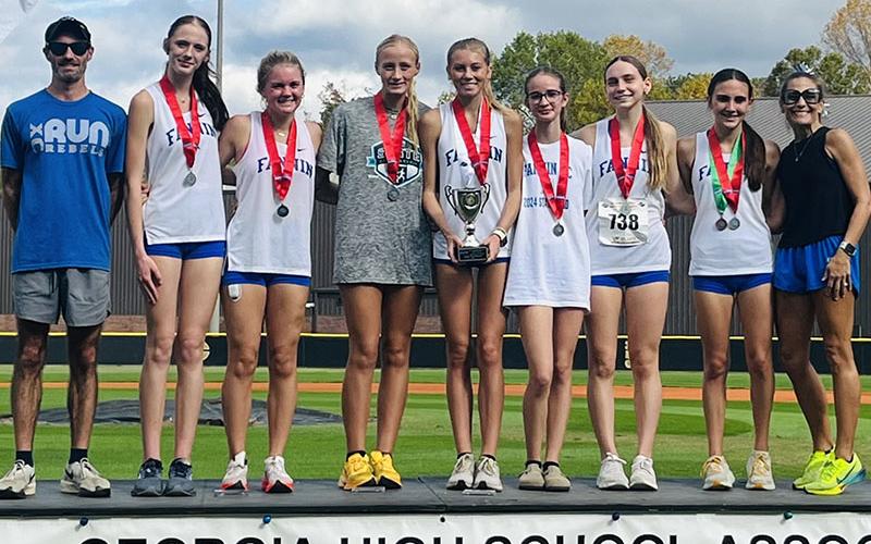 Celebrating the Fannin County High School girls cross country team runner-up victory on the podium after the event are, from left, Coach Dr. Lucas Roof, Lana Hicks, Annaleigh Cheatham, Kensley Pickelsimer, Lindsey Holloway, Sydney Ford, Lila Borum, Karli Sams and Coach Miranda Roof.