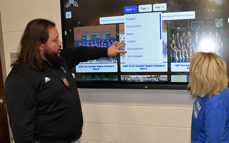 Fannin County High School (FCHS) Athletic Director Jeremy King explains an interactive sports history screen at the FCHS gym to Kelly Ledford, whose picture is already included in sports history.