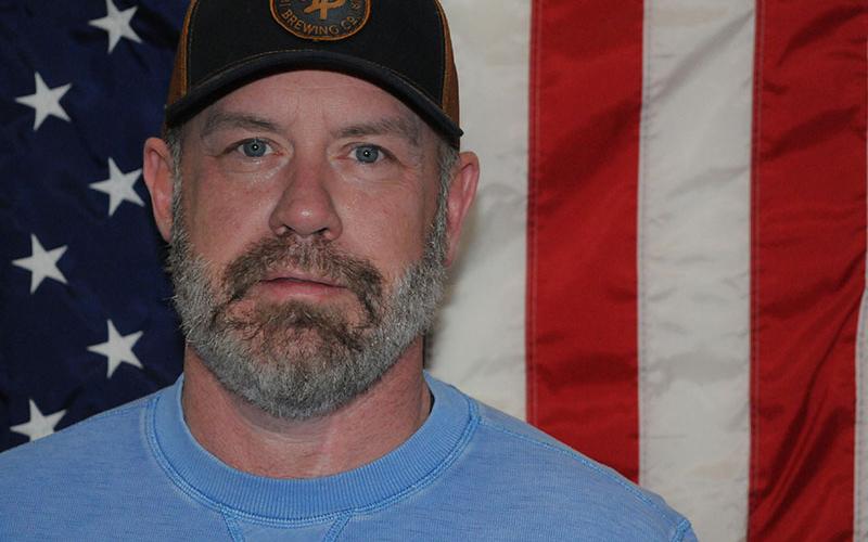 Former first battalion of the 108th Cavalry Regiment medic Aaron Born stands in front of an American flag.