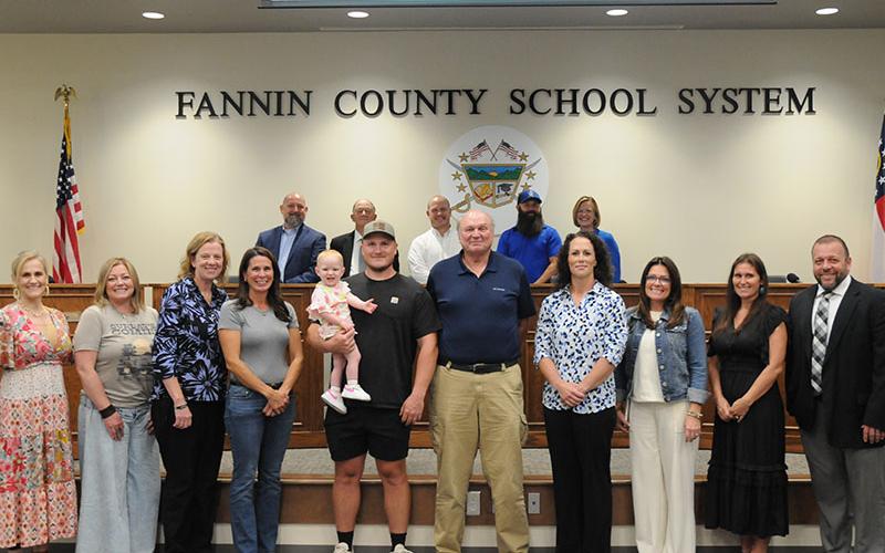 The new gym on the Fannin County High School campus will be named the Coach Johnny Farmer Gymnasium. The announcement came during the May 8 meeting of the Board of Education. Shown following the announcement are, from left, front, Dr. Connie Huff, Tara Queen, Suzianne Pass, Melissa Patton, Navy Grace held by Jordan Farmer, Farmer, Ashley H. Weeks, Shannon York, Brittney Stinnett, Dr. Scott Ramsey; and, back, Mike Cole, Bobby Bearden, Adam Born and Robert Patterson, and Shannon Dillard.
