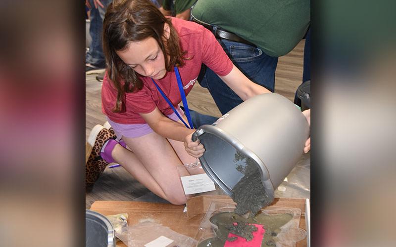 Charleigh Brown carefully pours the second layer of concrete into the mold for her memory stone. A first layer was poured into the mold, then children wrote a memory of a loved one they had lost, placed it on that layer, and added a second layer of concrete on top. The stone was then decorated to make it personal.