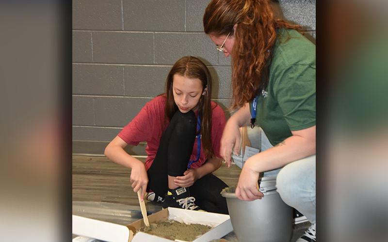 Makensley Bush spreads concrete into her mold under the watchful eye of Jasmine Green.