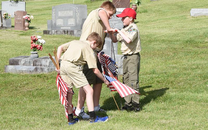 Boy Scouts from Troop 32 Max Benson, Grant Dilbeck and Ethan Threet, from left, honor a veteran by putting a flag on his grave in Crestlawn Cemetery.