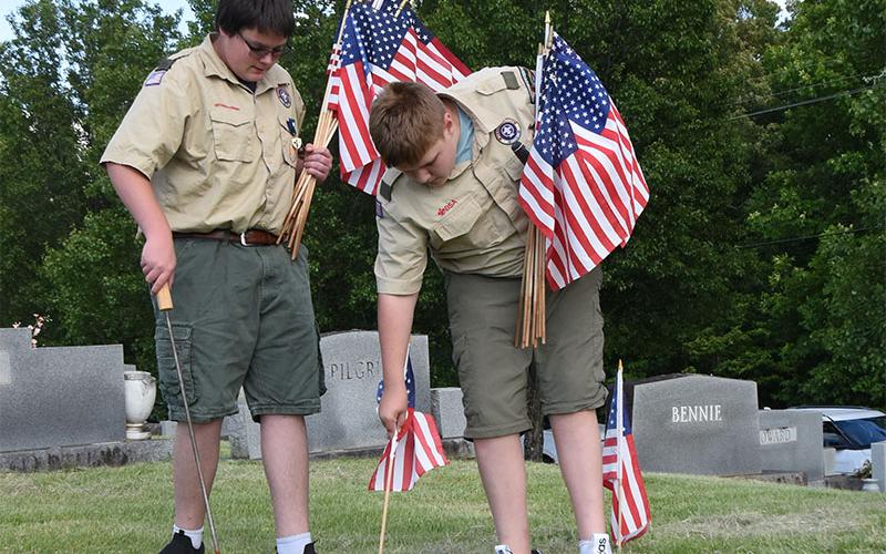 Patrick Cook, left, and Grant Dilbeck work to place a flag on a veteran’s grave in Crestlawn Cemetery.