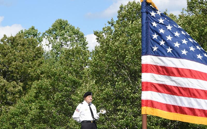 Bill Hall of the North Georgia Honor guard, framed by a United States flag, stands ready to play Taps as the ceremony to honor veterans with flags on graves began at Crestlawn Cemetery.