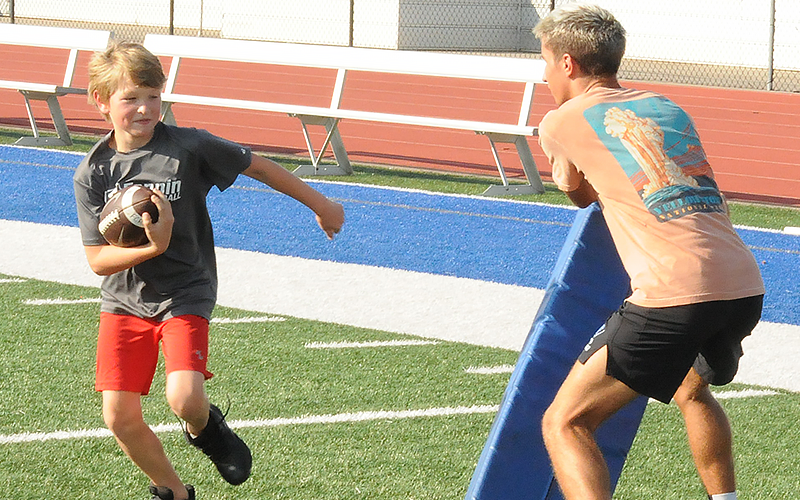 High school varsity Rebel Conrad Head teaches a young runner how to avoid a tackler.