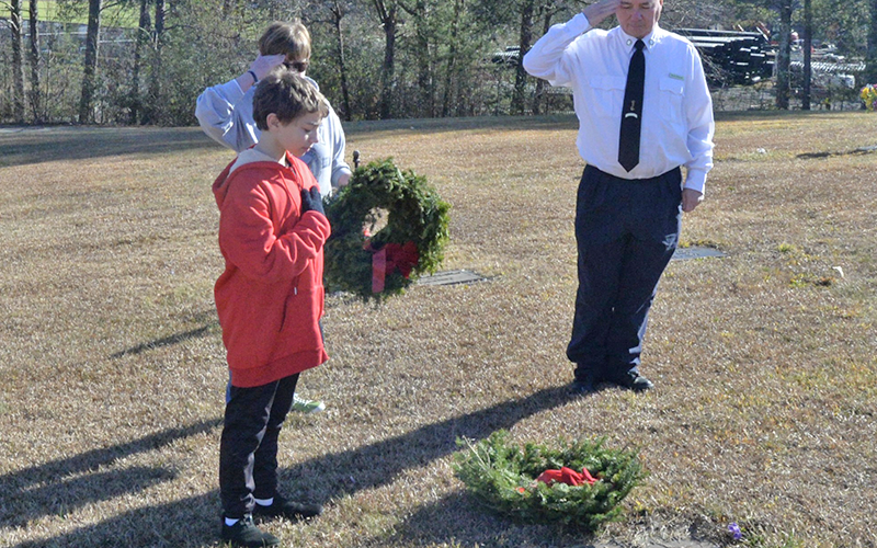 Sean O’Quinn, Pam Marsh and Kevin O’Quinn, from left, salute a veteran’s grave after placing a memorial wreath for the county’s Wreaths Across America event.
