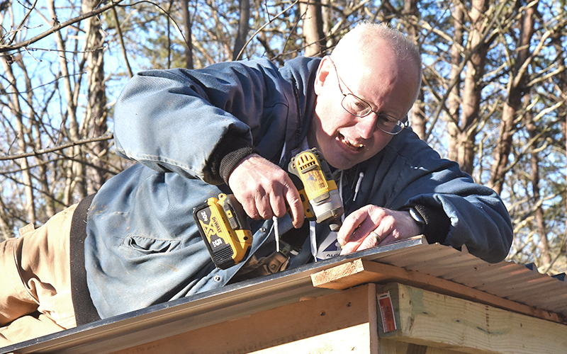 Freedom for Fido Co-Founder Fritz Gilbert secures the metal for a covered awning the volunteers built at their 200th fence build for the dog, Kie, to take shelter from rain and weather.