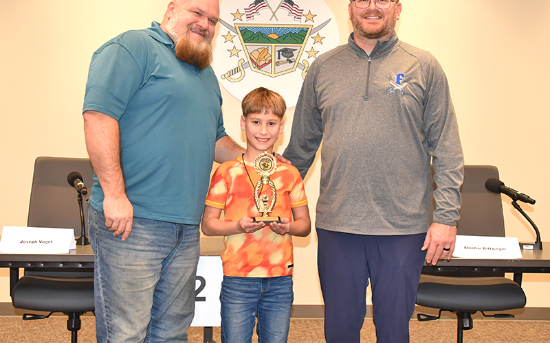 Abishai Rittweger was joined by his step dad, Charles Tucker, and East Fannin Elementary Principal Mathew Price, right, after he accepted his trophy for winning the Fannin County School District Spelling Bee last week.