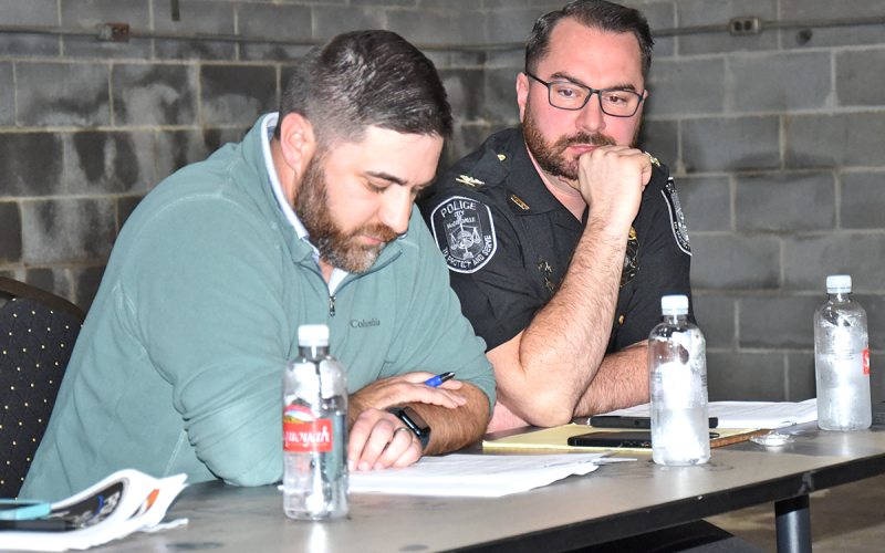 McCaysville City Councilman Jason Woody, left, reads a resolution calling for liquor by the drink to be decided by voters. Listening to Woody read a potential ballot question is Police Chief Michael Earley.