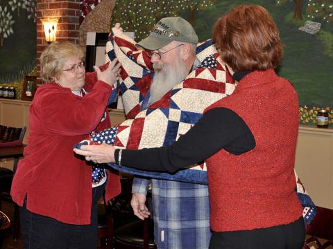 Susan Young with the Quilts of Valor Foundation, left, and quilter Robin Czyscon present U.S. Army veteran Chuck Bowen III with his own unique quilt Wednesday, January 29.