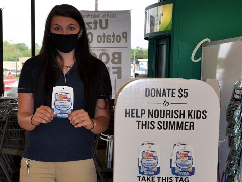 Blue Ridge’s Food Lion Customer Service Lead Helen Ramey holds up a hang tag for customers to grab if they want to contribute to Summers Without Hunger. Next to her is a display, right next to their CoinStar machine, where the tags may be found.