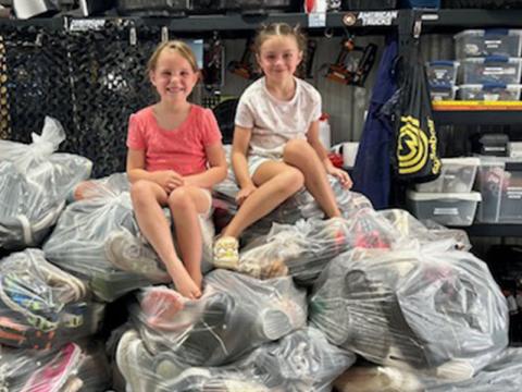 Hannah O’Neal, left, and Lily Suri sit on top of several bags of shoes collected at East Fannin Elementary’s shoe drive fundraiser. In total, 52 bags were collected.