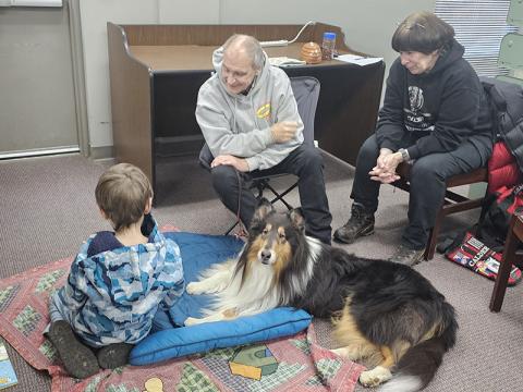 Leon Painter practices his reading skills with Calder at the Fannin County Public Library’s Book Buddies with Calder Reading Dog Program. Calder’s handlers Bill and Lois Hall are also shown.