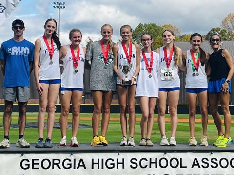 Celebrating the Fannin County High School girls cross country team runner-up victory on the podium after the event are, from left, Coach Dr. Lucas Roof, Lana Hicks, Annaleigh Cheatham, Kensley Pickelsimer, Lindsey Holloway, Sydney Ford, Lila Borum, Karli Sams and Coach Miranda Roof.