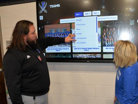 Fannin County High School (FCHS) Athletic Director Jeremy King explains an interactive sports history screen at the FCHS gym to Kelly Ledford, whose picture is already included in sports history.