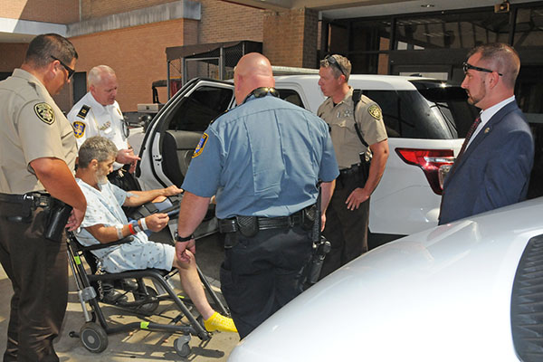 Law enforcement officers prepare to put James Larry Parris Jr., (in chair) into a McCaysville patrol vehicle outside WellStar Kennestone Hospital in Marietta last Thursday at noon. McCaysville officers shown are, Det. Capt. Billy Brackett, second from left; McCaysville Patrolman Mark Chastain, with back to camera; and McCaysville Police Chief Michael Earley, right.