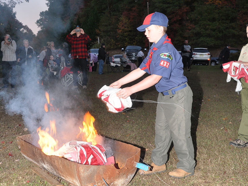 Eian Holloway, a Cub Scout with Pack 432, throws a tattered flag into the fire during the Flag Retirement ceremony at Ron Henry Horseshoe Bend Park Tuesday, October 22.