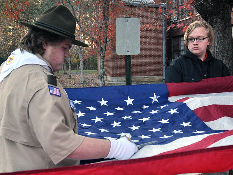 Jonothon Payne, assistant scout master for Ducktown Boy Scout Troop 14, cuts a large American flag stripe by stripe during a ceremony to properly retire old flags.Dakota Harris is shown helping hold the flag.