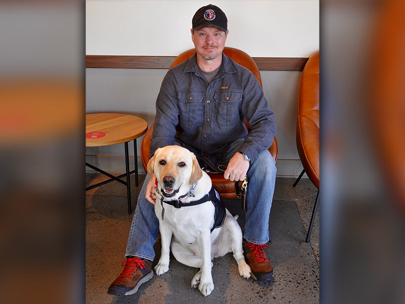 Retired U.S. Army Staff Sergent Stephen Fry Jr., sits with service dog Valor at one of his Operation Supply Drop Afghanistan checkpoints, Starbucks of Blue Ridge.