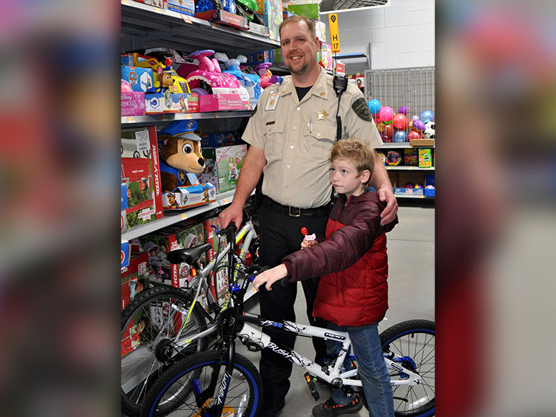 Fannin County Deputy Sheriff and School Resource Officer Jim Burrell smiles while Damian Long tests out a bicycle during Shop With A Cop. .