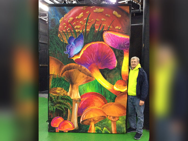 Enjoy the hand-painted murals by local artists while being entertained by the cast’s performance of Alice in Wonderland. The play began January 24 and will continue through February 9. Shown is Larry Minor standing next his mural of fantastical mushrooms.