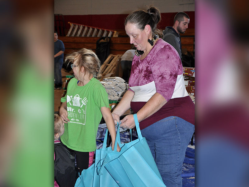 Volunteer Carrie Beaver holds reusable bags while a young volunteer fills them with peanut butter and tomato sauce.