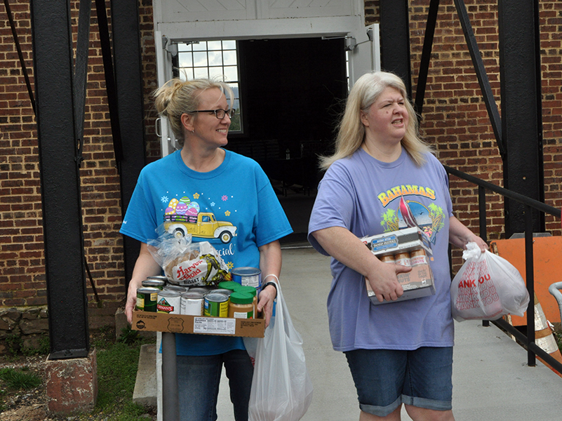 Amanda Pittman, left and Jill Crago Rose carry food and supplies to vehicles during the March 19 food distribution.