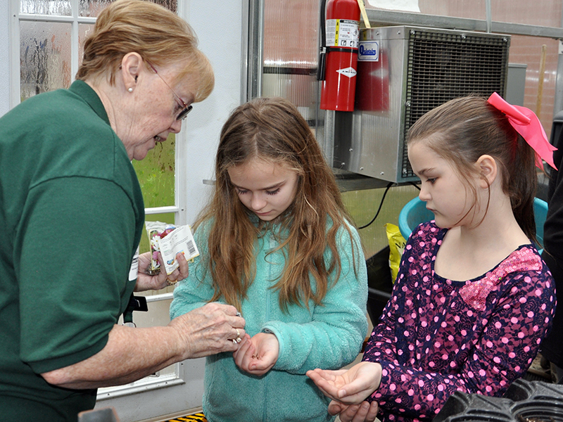 Master Gardener Denise Atkins, left, carefully places a few seeds in the hands of East Fannin Elementary students Mallory Cline, center, and Cora Burnette during a special class Monday, March 3.