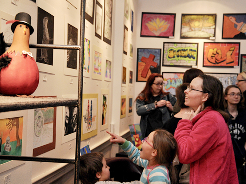 Charity Roderick, an 8-year-old homeschool student and award winner in the homeschool division, admires the artwork on display at Blue Ridge Mountains Arts Association’s Youth Art Month opening reception Thursday, February 27. She is accompanied by mother Jennifer and brother Charlie.