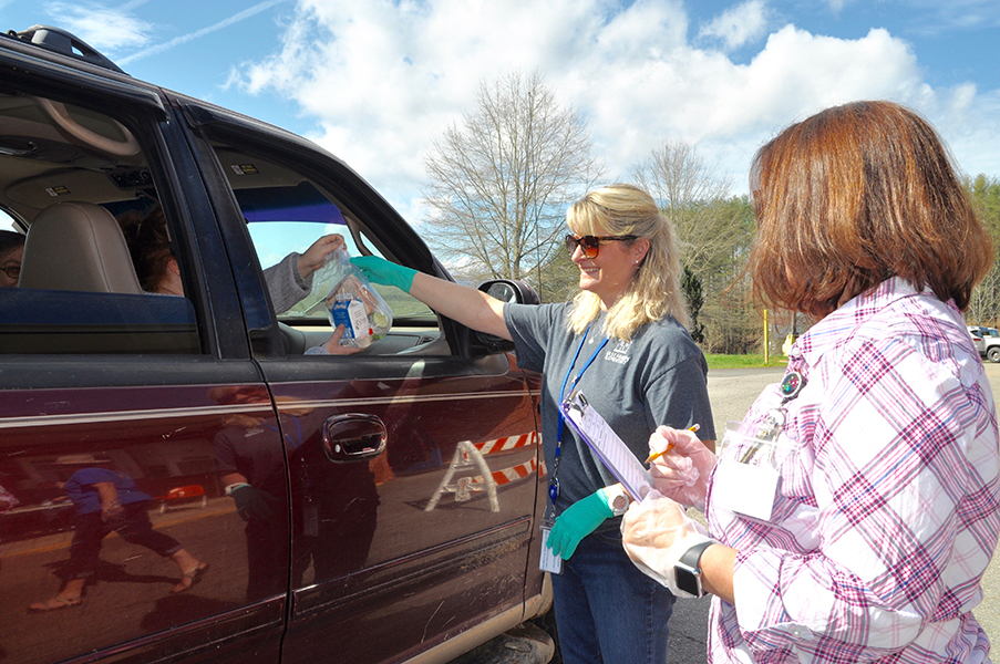 East Fannin Elementary School teacher Kathy Culpepper hands a pre-packaged meal to a Fannin County family, while teacher Christie Holtman documents it, during the school closure caused by COVID-19.
