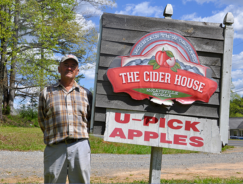 Mountain View Orchards Founder Joe Dickey stands beside a sign carrying a logo for the former restaurant.