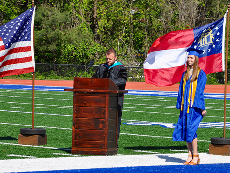 Abigail O’Neal stands ready before walking the Fannin County High School football field to receive her diploma during a private graduation ceremony. Assistant Principal Scott Ramsey stands at the podium to announce each graduate.