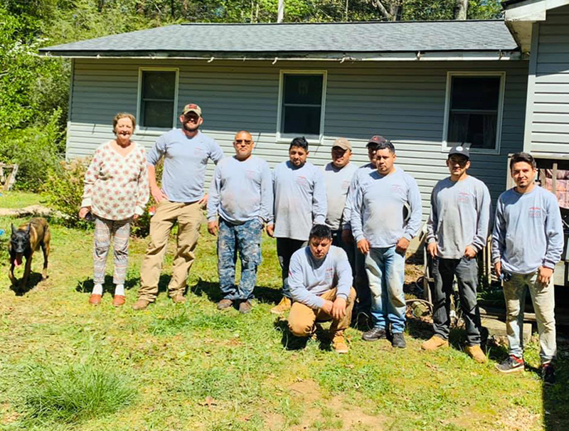 Virginia Card stands beside Semper Fi Roofing and Restoration Owner Nick Black and workers while having her roof repaired.