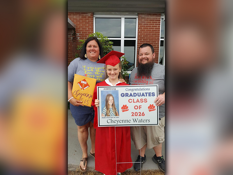 CBES graduate Cheyenne Waters smiles as she shows off her sign with teachers Jennifer Speights and Andrew Cook.