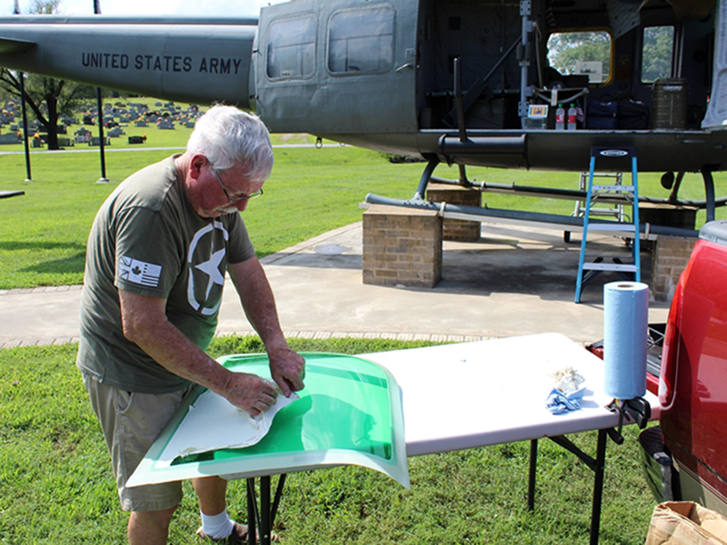 Veteran Rod McIntyre is shown peeling off the protective spraylat coating of the new greenhouse window for the Huey helicopter that was recently damaged.