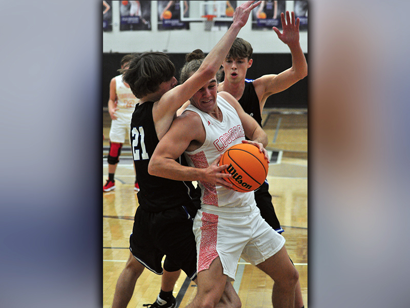 Cougar Radford Cheek (11) muscles through Rebels Nick Arp (21) and Kaeden Twiggs (5) during the Rebels and Cougars basketball game Tuesday, November 24.