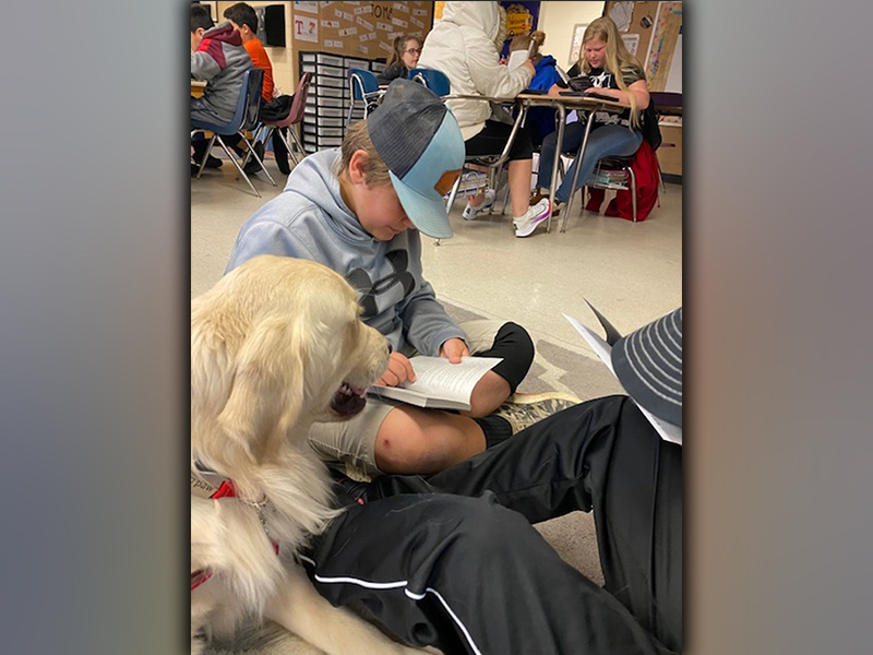 Charlie sits patiently while a young boy reads to him during a school visit.