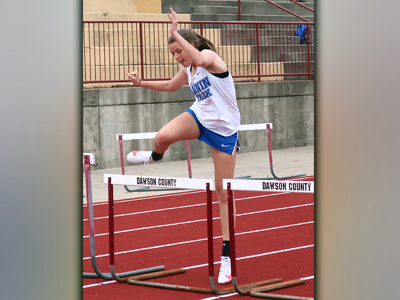 Lady Rebel Macy Hawkins jumps over a hurdle in the 200 meter event at the Dawson County tri-meet between the Rebels, Tigers and Johnson High School. Hawkins placed second in the event and finished with a time of 26.91.