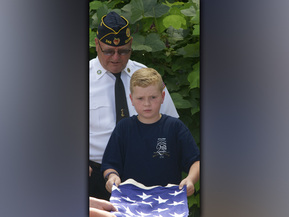 Blue Ridge Elementary School fifth grade student Owen Norton folds an American Flag properly while North Georgia Honor Guard member Richard Crosley instructs from behind.