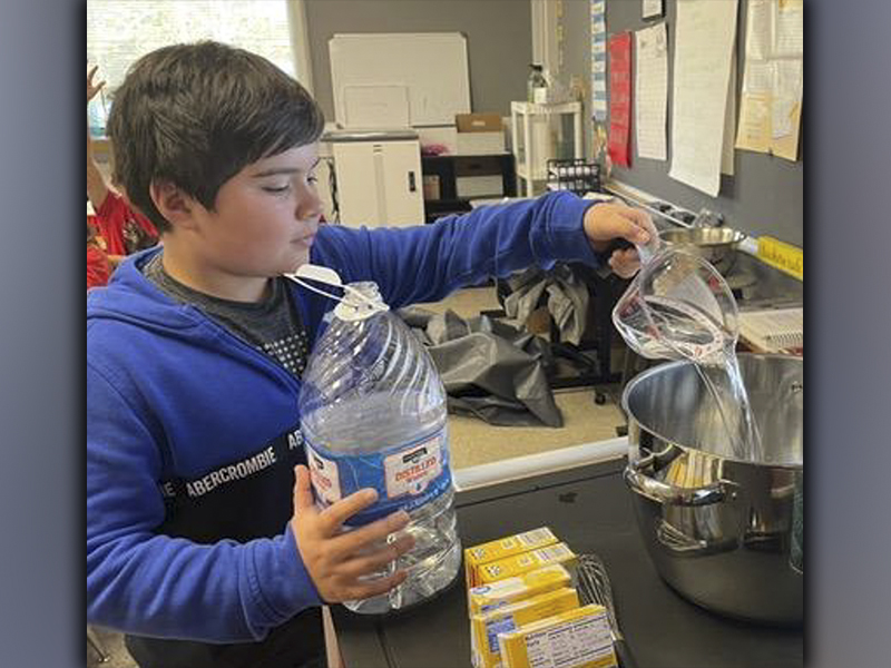 Grayson Woody adds water to the gelatin mixture in order to make pineapple flan as part of a lesson with fourth-grade students at West Fannin Elementary School that tied in several school subjects.
