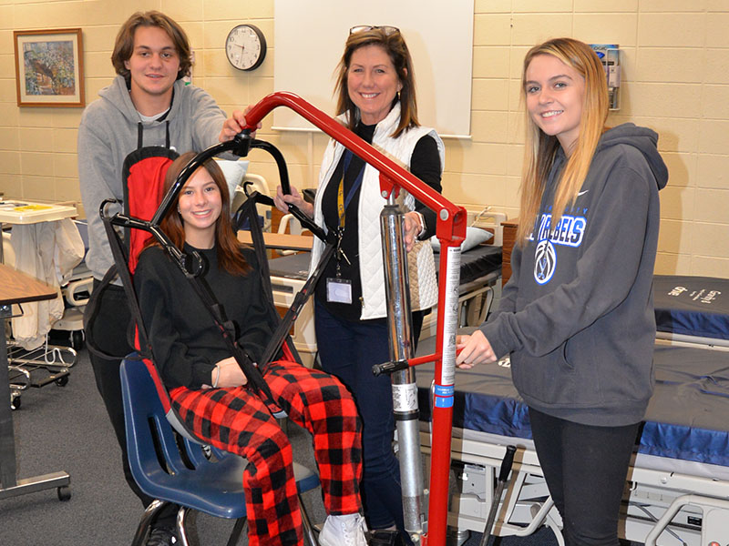 Certified Nursing Assistant (CNA) students at Fannin County High School learn to use a patient lift to move patients from a bed to a chair as part of their training. Demonstrating the equipment are, from left, Michael Treon, Devan Hogsed (seated), instructor Anne Gibbs and Riley Reeves.