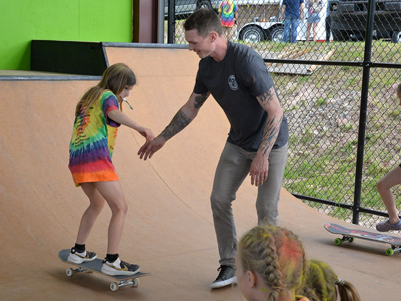 Austin Leach, director of Highland Outdoor Ministry, works with a young skater as she learns how to ride a skate board at Syd’s Place.